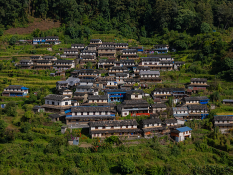 Aerial view of a traditional mountain village with stone houses dark slate roofs and terraced fields nestled in lush green hills Nepal.