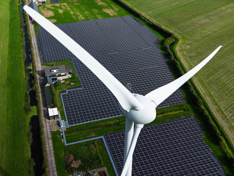 Aerial view of a wind turbine beside a large solar panel farm and house surrounded by green agricultural fields and irrigation canals in t Zand North Holland Netherlands. Aerial view of a wind turbine beside a large solar panel farm and house surrounded by green agricultural fields and irrigation canals in t Zand North Holland Netherlands.