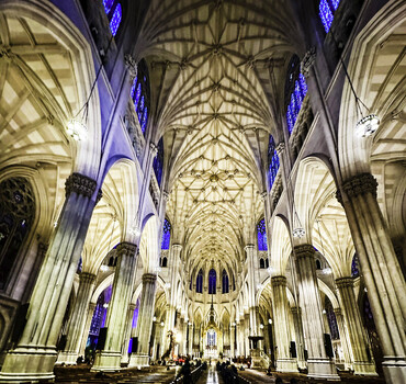 View of the ornate vaulted ceiling towering stone columns and stained glass windows inside St. Patrick s Cathedral in New York New York United States.