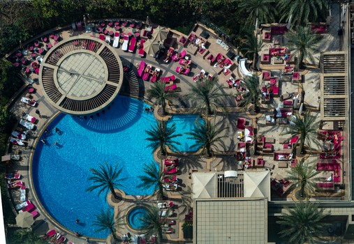 View of a luxury resort swimming pool with turquoise water palm trees and people relaxing on pink lounge chairs in Dubai Dubai United Arab Emirates. View of a luxury resort swimming pool with turquoise water palm trees and people relaxing on pink lounge chairs in Dubai Dubai United Arab Emirates.