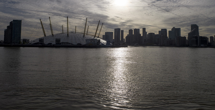 Aerial view of The Millennium Dome on the banks of the River Thames with the Canary Wharf skyline in the background under a cloudy sky in London England United Kingdom. Aerial view of The Millennium Dome on the banks of the River Thames with the Canary Wharf skyline in the background under a cloudy sky in London England United Kingdom.