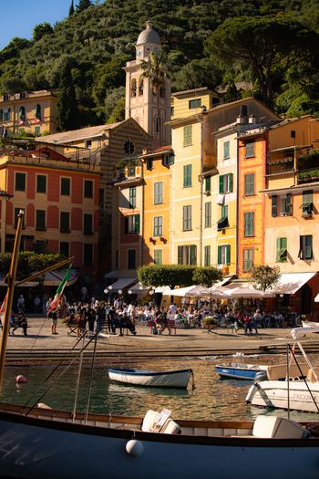 View of the colorful historic buildings and outdoor cafes at the harbor with small boats and the church bell tower Portofino Liguria Italy.