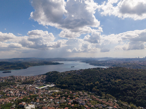 Aerial view of the Bosphorus featuring green hills residential neighborhoods and cargo ships navigating the waterway under a bright sky in Istanbul Istanbul Turkiye.