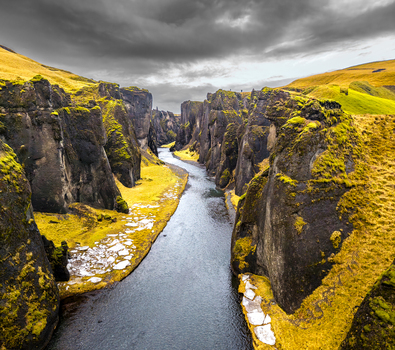 Aerial view of a deep river canyon carved through mossy cliffs under a dramatic sky Fjaðrárgljúfur Iceland. Aerial view of a deep river canyon carved through mossy cliffs under a dramatic sky Fjaðrárgljúfur Iceland.