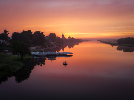 Aerial view of the Meuse river at sunrise with a ferry docked by the shore and a church spire on the horizon in Kessel Limburg Netherlands.