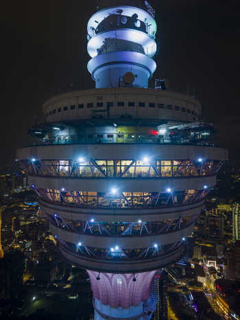 Kuala Lumpur Malaysia 11 March 2026 Aerial view of the illuminated Menara Kuala Lumpur tower at night with people visible in the observation decks against the city skyline.