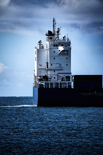View of a large cargo ship navigating through the deep blue ocean waters under a cloudy sky.