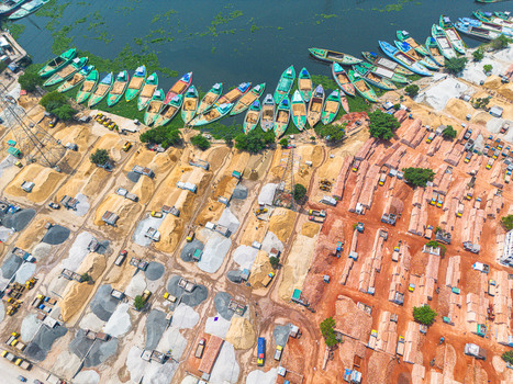 Aerial view of boats docked along the murky river s edge beside piles of sand and brick in contrasting earthy tones Dhaka Dhaka Division Bangladesh. Aerial view of boats docked along the murky river s edge beside piles of sand and brick in contrasting earthy tones Dhaka Dhaka Division Bangladesh.