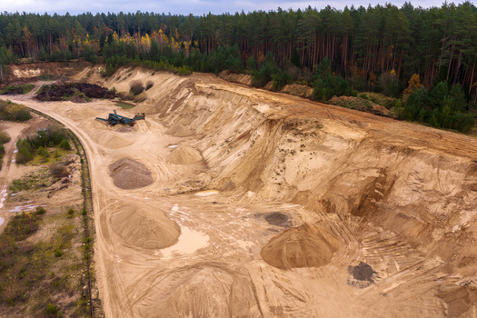 Aerial view of a sand quarry with excavation machinery and piles of sand surrounded by a dense pine forest in Nemencine Vilnius County Lithuania. Aerial view of a sand quarry with excavation machinery and piles of sand surrounded by a dense pine forest in Nemencine Vilnius County Lithuania.