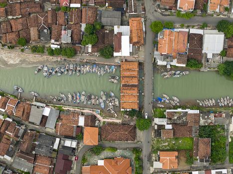 Aerial view of boats docked along the river juxtaposed against the rustic red rooftops of the buildings creating a vibrant tapestry of urban life Jepara Central Java Indonesia.