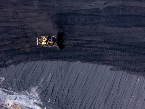 Aerial view of a bulldozer working on a large coal pile at a power plant with visible tracks in the dark surface in West Olive Michigan United States. Aerial view of a bulldozer working on a large coal pile at a power plant with visible tracks in the dark surface in West Olive Michigan United States.