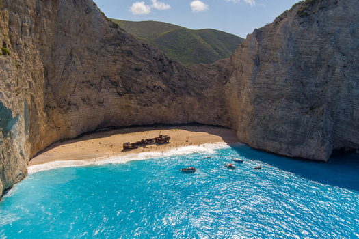 Aerial view of Navagio beach featuring the iconic shipwreck on the sand surrounded by towering limestone cliffs and turquoise waters with small boats in Zakynthos Navagio Greece.