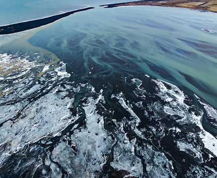 Aerial view of the intricate glacial river delta with black sand deposits and icy blue water channels flowing into the sea in Iceland. Aerial view of the intricate glacial river delta with black sand deposits and icy blue water channels flowing into the sea in Iceland.