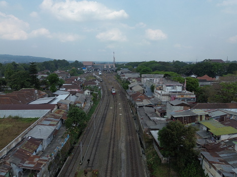 Aerial view of Stasiun Malang Kota Baru with railway tracks running through the urban neighborhood surrounded by rooftops and lush trees in Kecamatan Klojen Jawa Timur Indonesia.