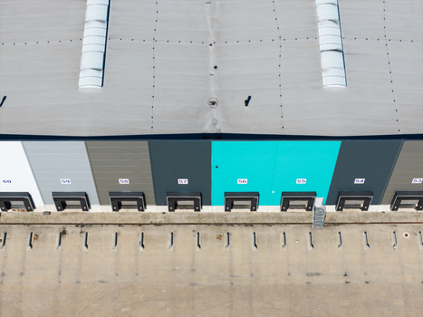 Aerial view of a modern warehouse facility featuring multiple numbered loading docks a flat roof with skylights and a paved yard in Lielvarzi Kekava Municipality Latvia. Aerial view of a modern warehouse facility featuring multiple numbered loading docks a flat roof with skylights and a paved yard in Lielvarzi Kekava Municipality Latvia.