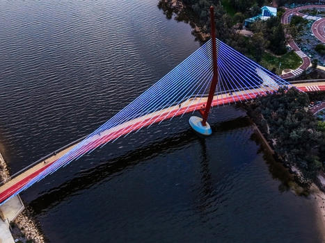 Aerial view of Boorloo Bridge spanning the Swan River with its distinctive red arch and blue lighting surrounded by parklands and pathways in East Perth Western Australia Australia.