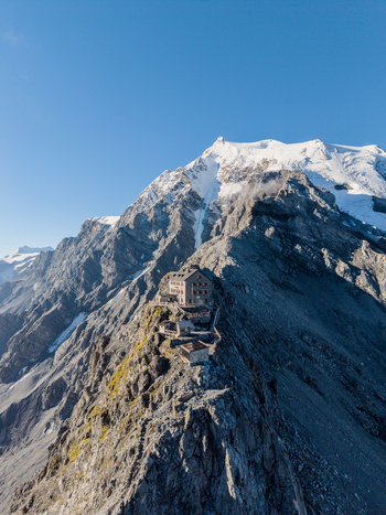 Aerial view of Payerhutte perched on a rocky ridge with the snow capped Ortler Mountain in the background under a clear blue sky in Stilfs Trentino Alto Adige Italy. Aerial view of Payerhutte perched on a rocky ridge with the snow capped Ortler Mountain in the background under a clear blue sky in Stilfs Trentino Alto Adige Italy.