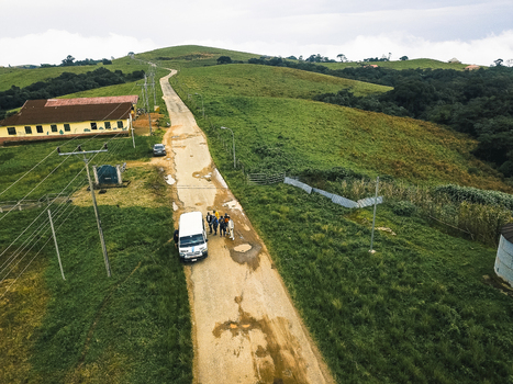 Aerial view of a winding dirt road through lush green hills past a yellow brown building and a white van with people Obudu Cross River Nigeria.