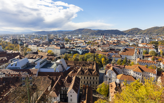 View of rooftops cascading towards a distant skyline under a vast blue sky dotted with fluffy clouds a scenic panorama of urban architecture Graz Styria Austria. View of rooftops cascading towards a distant skyline under a vast blue sky dotted with fluffy clouds a scenic panorama of urban architecture Graz Styria Austria.