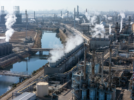 Aerial view of an industrial oil refinery complex featuring cooling towers emitting steam pipe networks and a canal running through the facility in Carson California United States.