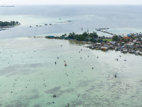 Aerial view of a coastal village nestled against turquoise waters with fishing boats scattered across the sea Karimunjawa Central Java Indonesia. Aerial view of a coastal village nestled against turquoise waters with fishing boats scattered across the sea Karimunjawa Central Java Indonesia.