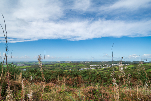 View of the rolling landscape and clay pits near St Austell with green hills distant town buildings and foreground vegetation under a blue sky in St Austell Cornwall United Kingdom. View of the rolling landscape and clay pits near St Austell with green hills distant town buildings and foreground vegetation under a blue sky in St Austell Cornwall United Kingdom.
