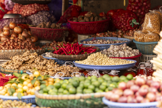 View of a vibrant market stall displaying baskets of fresh ginger red chilies garlic limes and onions Hanoi Ha Noi Vietnam.