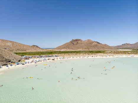 Aerial view of Balandra beach with turquoise shallow water sandy shore and people relaxing under umbrellas surrounded by arid hills in La Paz Baja California Sur Mexico. Aerial view of Balandra beach with turquoise shallow water sandy shore and people relaxing under umbrellas surrounded by arid hills in La Paz Baja California Sur Mexico.