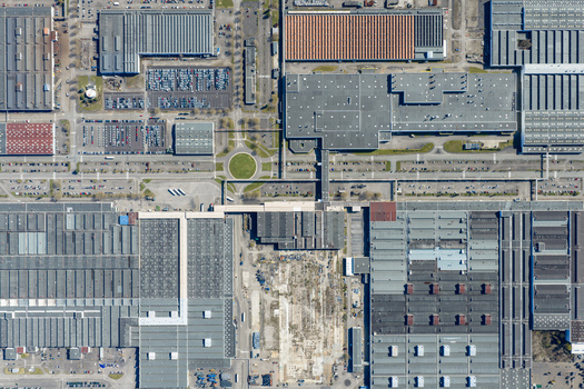 Aerial view of vast industrial rooftops casting shadows a symphony of geometric shapes and textures with a roundabout providing a touch of green amidst the concrete Sausheim Grand Est France.