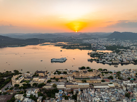Aerial view of the City Palace and Lake Pichola at sunset with historic architecture calm waters and distant hills in Udaipur Rajasthan India.