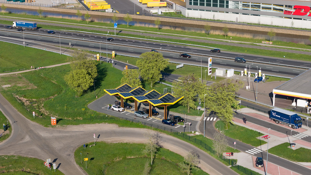 Bant Netherlands 23 April 2026 Aerial view of the Fastned Charging Station with electric cars parked under the yellow solar roof next to a busy highway and green fields. Bant Netherlands 23 April 2026 Aerial view of the Fastned Charging Station with electric cars parked under the yellow solar roof next to a busy highway and green fields.