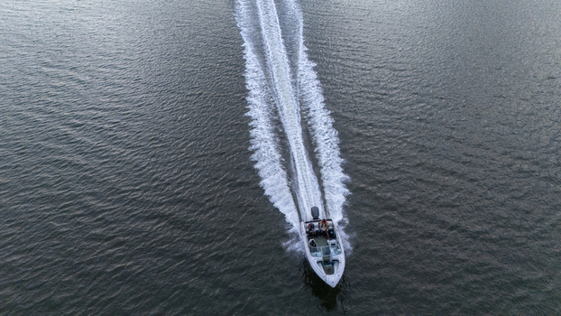 Aerial view of a motorboat cruising through dark water with people on board and a long white wake trailing behind Badagry Lagos Nigeria. Aerial view of a motorboat cruising through dark water with people on board and a long white wake trailing behind Badagry Lagos Nigeria.