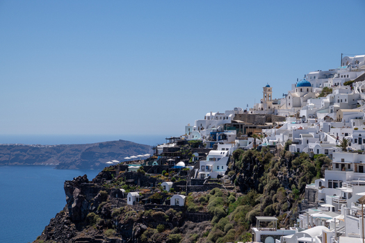 View of white houses and blue domed churches on the volcanic cliffs of Santorini overlooking the Aegean Sea under a clear blue sky Fira Greece. View of white houses and blue domed churches on the volcanic cliffs of Santorini overlooking the Aegean Sea under a clear blue sky Fira Greece.
