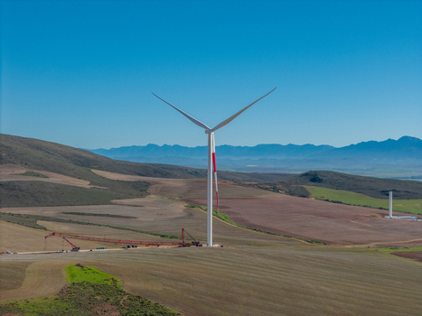 Aerial view of a large wind turbine standing in rolling agricultural fields with distant mountains under a clear blue sky in Swellendam Western Cape South Africa. Aerial view of a large wind turbine standing in rolling agricultural fields with distant mountains under a clear blue sky in Swellendam Western Cape South Africa.