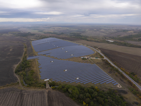 Aerial view of a large solar farm with rows of photovoltaic panels situated in a rural landscape with fields and a road in Bulgaria. Aerial view of a large solar farm with rows of photovoltaic panels situated in a rural landscape with fields and a road in Bulgaria.
