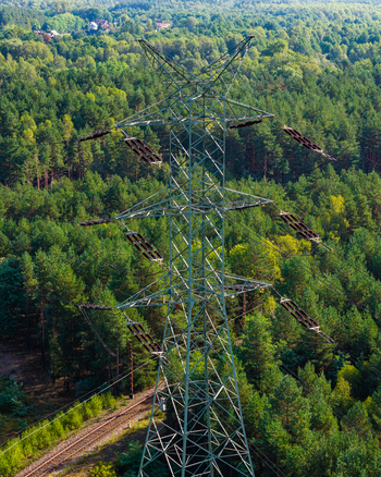 Aerial view of a high voltage power line pylon standing amidst a dense green forest with a railway track running below in Katowice Silesian Voivodeship Poland.
