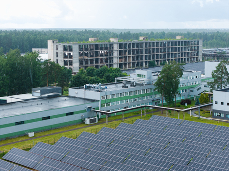 Olaine parish Latvia 04 July 2026 Aerial view of a solar panel array with modern industrial buildings and an abandoned concrete structure surrounded by green trees and forest. Olaine parish Latvia 04 July 2026 Aerial view of a solar panel array with modern industrial buildings and an abandoned concrete structure surrounded by green trees and forest.