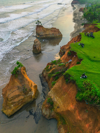 Aerial view of dramatic coastal cliffs with lush green grass unique rock formations in the sea and people enjoying the sunset view in Bali Bali Indonesia. Aerial view of dramatic coastal cliffs with lush green grass unique rock formations in the sea and people enjoying the sunset view in Bali Bali Indonesia.