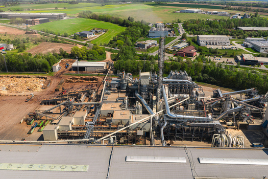 Aerial view of an industrial wood processing facility with complex piping and conveyor belts surrounded by green fields in Jihlava Vysocina Region Czechia.