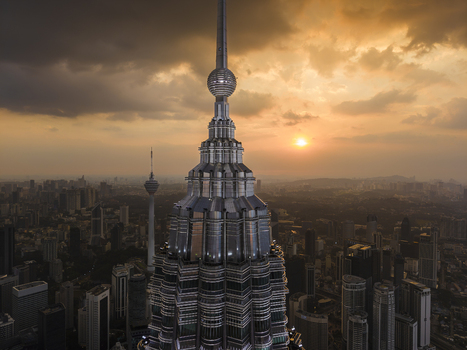 Kuala Lumpur Malaysia 11 March 2026 Aerial view of the Petronas Twin Towers spire at sunset with the city skyline and KL Tower under a dramatic cloudy sky.