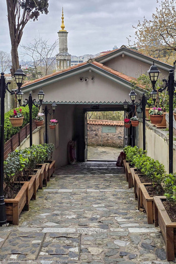 View of a stone paved walkway lined with wooden planters and vintage street lamps leading to a covered entrance with a minaret in the background Sariyer Istanbul Turkiye.
