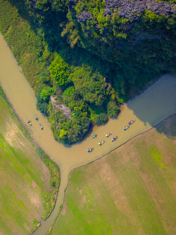 Aerial view of small boats navigating a winding river through lush green fields and dramatic karst rock formations in Vietnam. Aerial view of small boats navigating a winding river through lush green fields and dramatic karst rock formations in Vietnam.