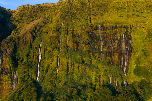 Aerial view of Poco da Ribeira do Ferreiro with multiple waterfalls cascading down lush green cliffs during golden hour in Fajazinha Azores Portugal. Aerial view of Poco da Ribeira do Ferreiro with multiple waterfalls cascading down lush green cliffs during golden hour in Fajazinha Azores Portugal.
