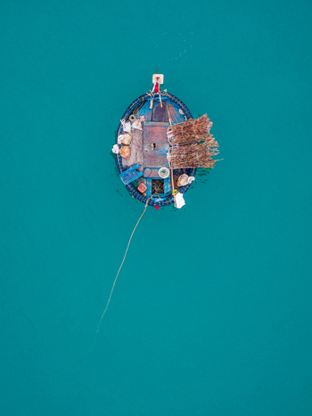 Aerial view of a traditional Vietnamese basket boat floating on calm turquoise water with fishing gear and nets on board in Vietnam. Aerial view of a traditional Vietnamese basket boat floating on calm turquoise water with fishing gear and nets on board in Vietnam.