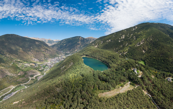 Aerial view of Lake Engolasters surrounded by dense pine forests and rugged mountain slopes with a valley town visible in the distance Encamp Andorra. Aerial view of Lake Engolasters surrounded by dense pine forests and rugged mountain slopes with a valley town visible in the distance Encamp Andorra.