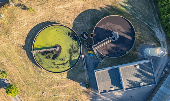 Aerial view of circular clarifier tanks at a wastewater treatment plant with green and dark water industrial buildings and grassy fields in Le Pouzin Auvergne Rhone Alpes France.