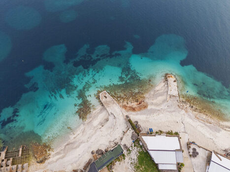 Aerial view of the turquoise waters and sandy coastline of Ksamil with a small pier and white buildings along the shore in Ksamil Vlore County Albania. Aerial view of the turquoise waters and sandy coastline of Ksamil with a small pier and white buildings along the shore in Ksamil Vlore County Albania.