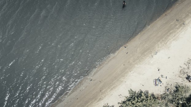 Aerial view of the shoreline with dark rippling water a sandy beach and a person wading near the edge in Badagry Lagos Nigeria.