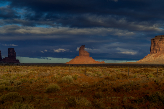 View of Monument Valley Tribal Park with dramatic sandstone buttes illuminated by golden light against a dark stormy sky in Oljato Monument Valley Utah United States.