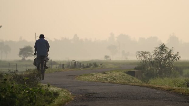 View of a man riding a bicycle on a misty rural road Bangladesh.